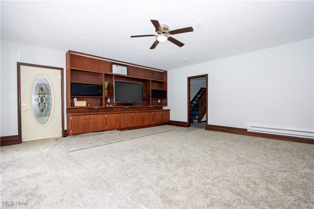 Unfurnished living room with a wall mounted air conditioner, a baseboard radiator, light colored carpet, and ceiling fan