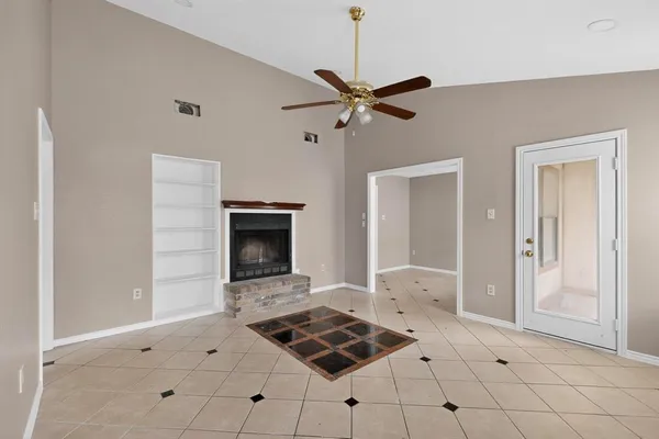 a view of an empty room with chandelier fan and fire place