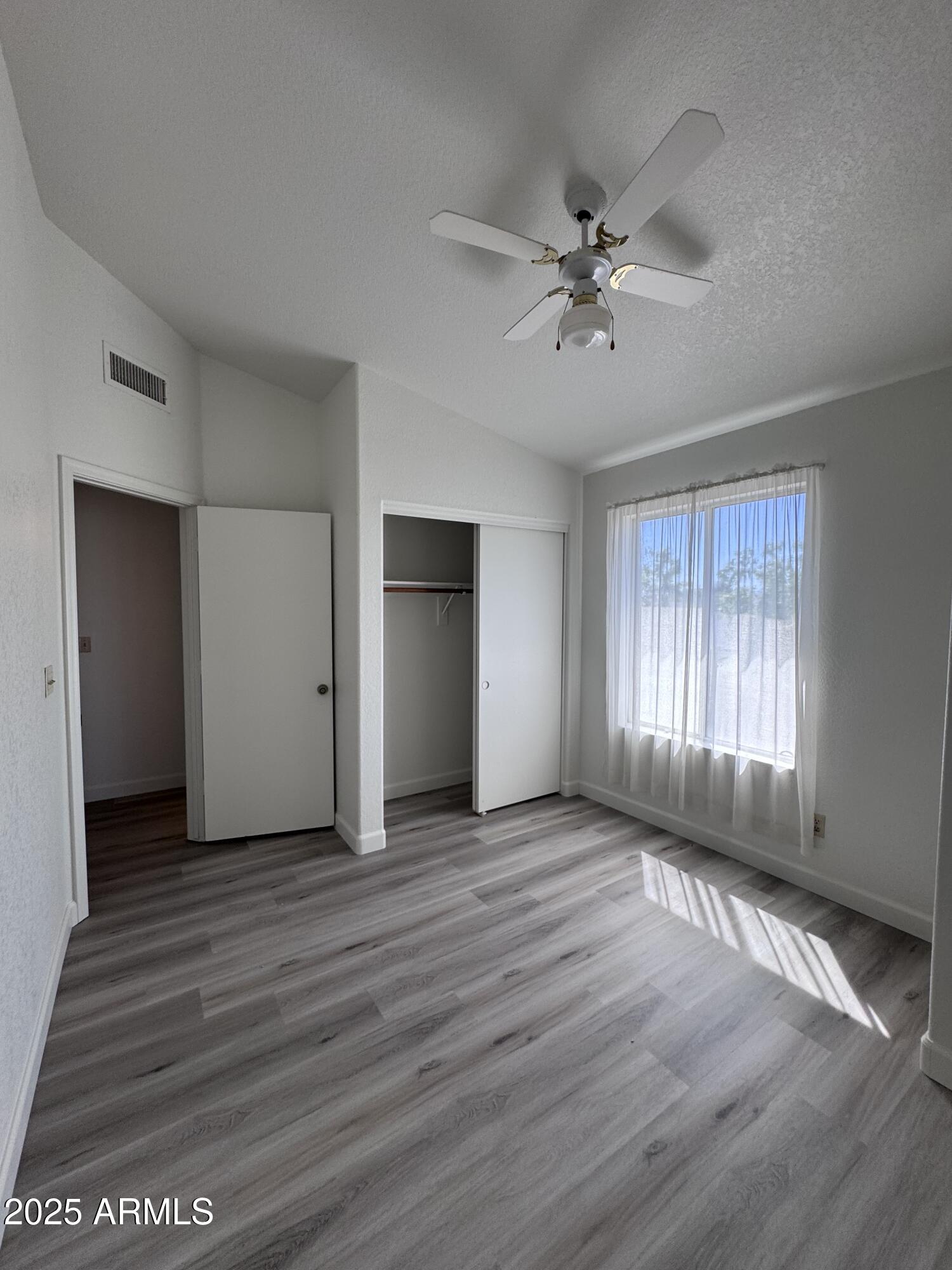 8631 West Monte Vista Road Phoenix, AZ 85037 - Photo 20 of 26 an empty room with wooden floor fan and windows