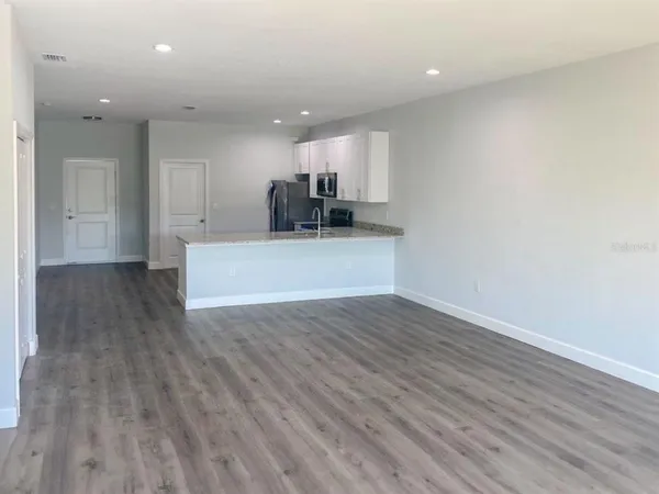 a view of kitchen and empty room with wooden floor