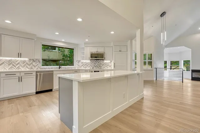 a kitchen with stainless steel appliances kitchen island granite countertop a stove a sink a refrigerator and white cabinets with wooden floor