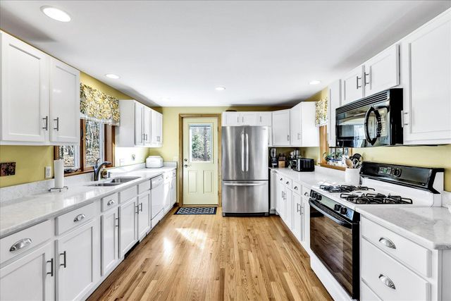 a kitchen with granite countertop a refrigerator a sink dishwasher a stove top oven a refrigerator and white cabinets with wooden floor