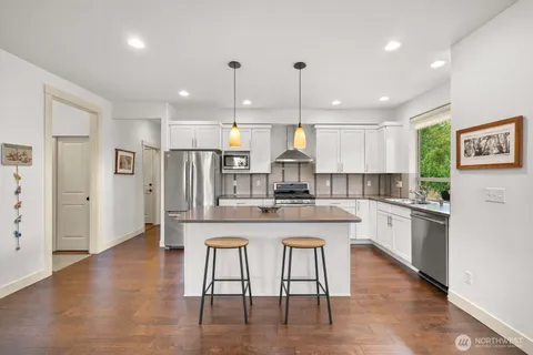 a kitchen with stainless steel appliances granite countertop a refrigerator a sink dishwasher a stove and white cabinets with wooden floor