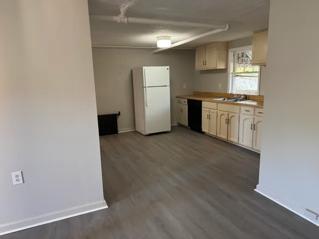 an empty room with wooden floor kitchen view and a window