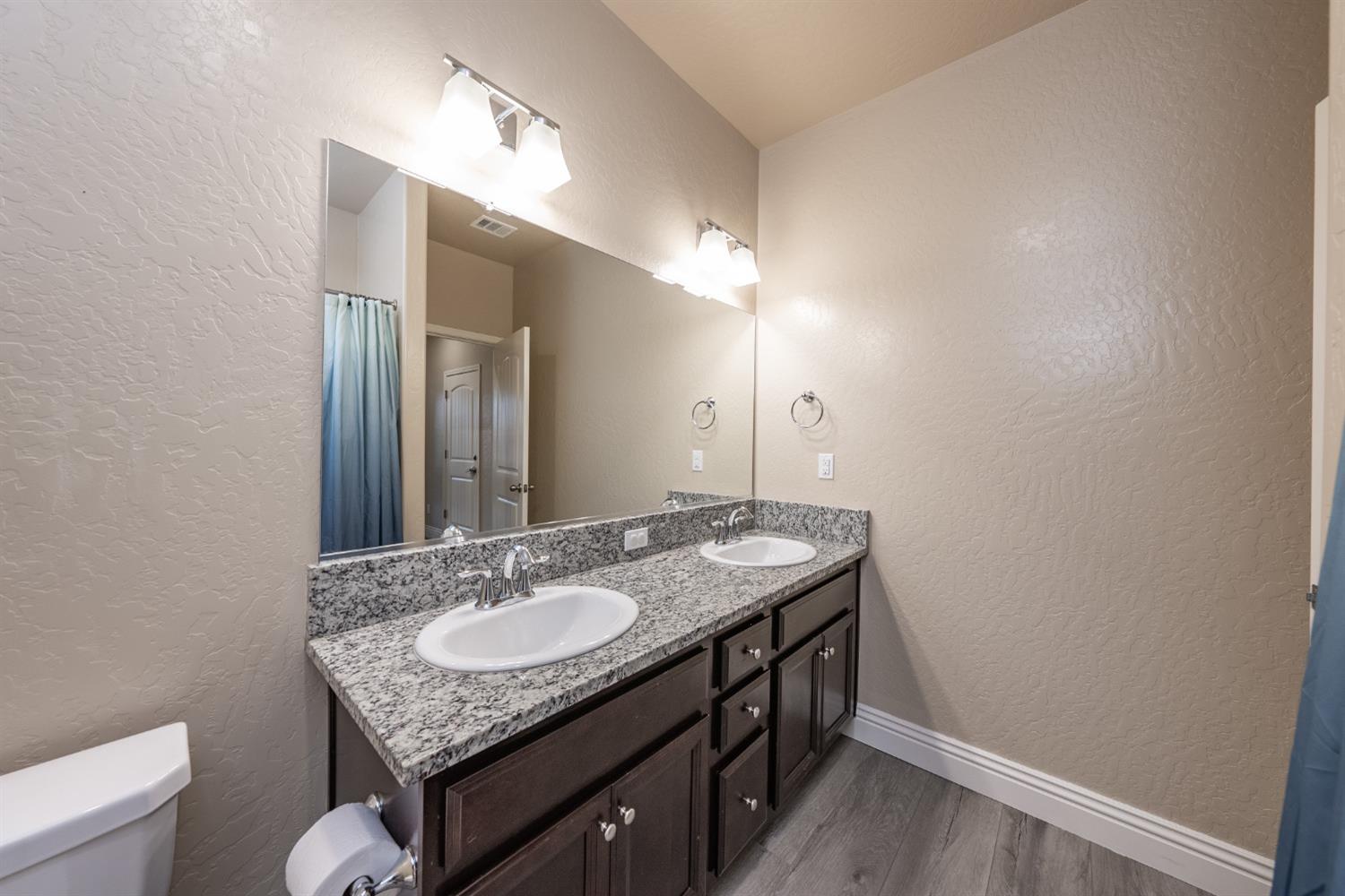 742 Strada Street Lemoore, CA 93245 - Photo 24 of 40 a bathroom with a granite countertop sink a toilet and a mirror