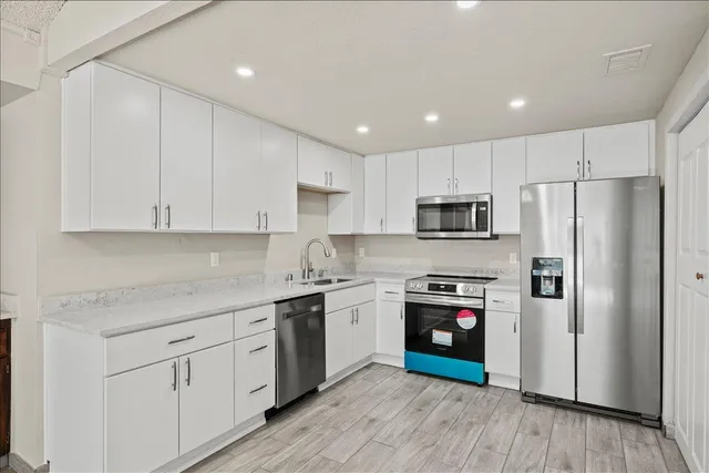 a kitchen with stainless steel appliances granite countertop a refrigerator a stove top oven a sink and dishwasher with wooden floor