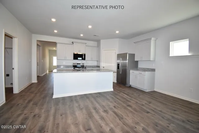 a large kitchen with stainless steel appliances granite countertop a stove a sink a refrigerator and white cabinets with wooden floor