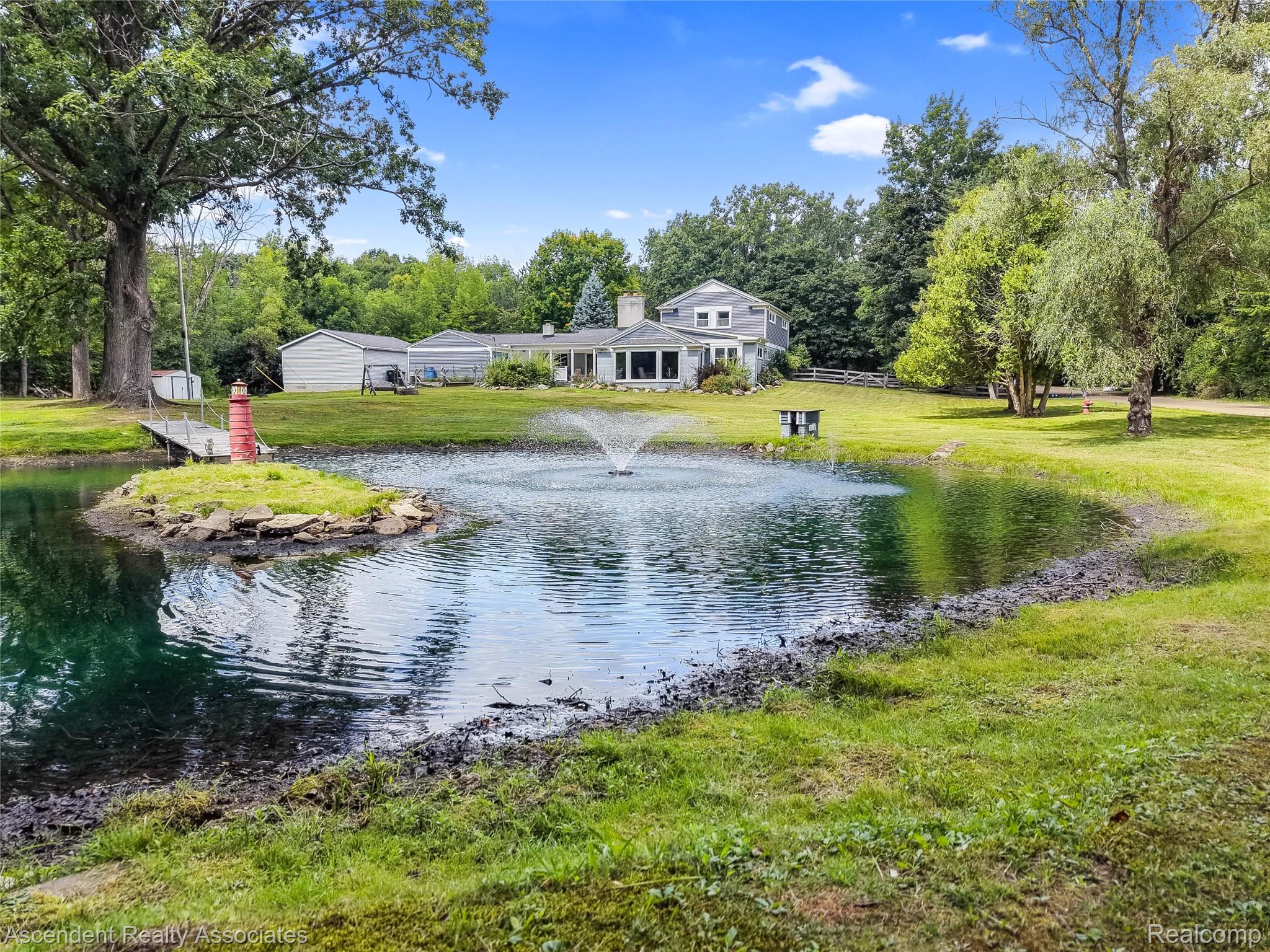 6157 Blue Beech Court Rochester, MI 48306 - Photo 3 of 30 Expansive outdoor grounds featuring a large pond with a fountain, a small island, and a decorative lighthouse