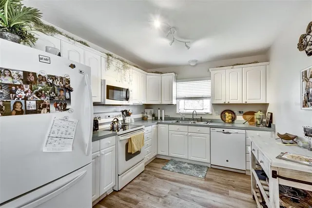 a kitchen with stainless steel appliances granite countertop a stove top oven a sink a refrigerator white cabinets and wooden floor