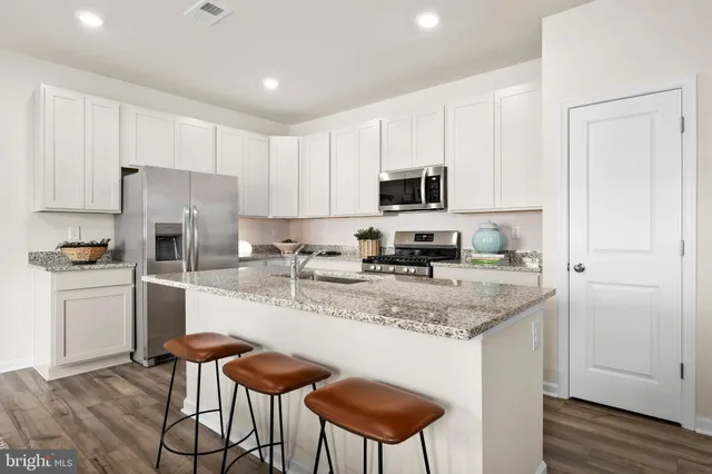 a kitchen with stainless steel appliances granite countertop a stove a sink a microwave a refrigerator and white cabinets