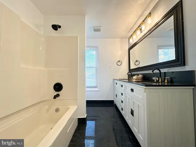 a bathroom with a granite countertop sink a mirror a bathtub and a shower