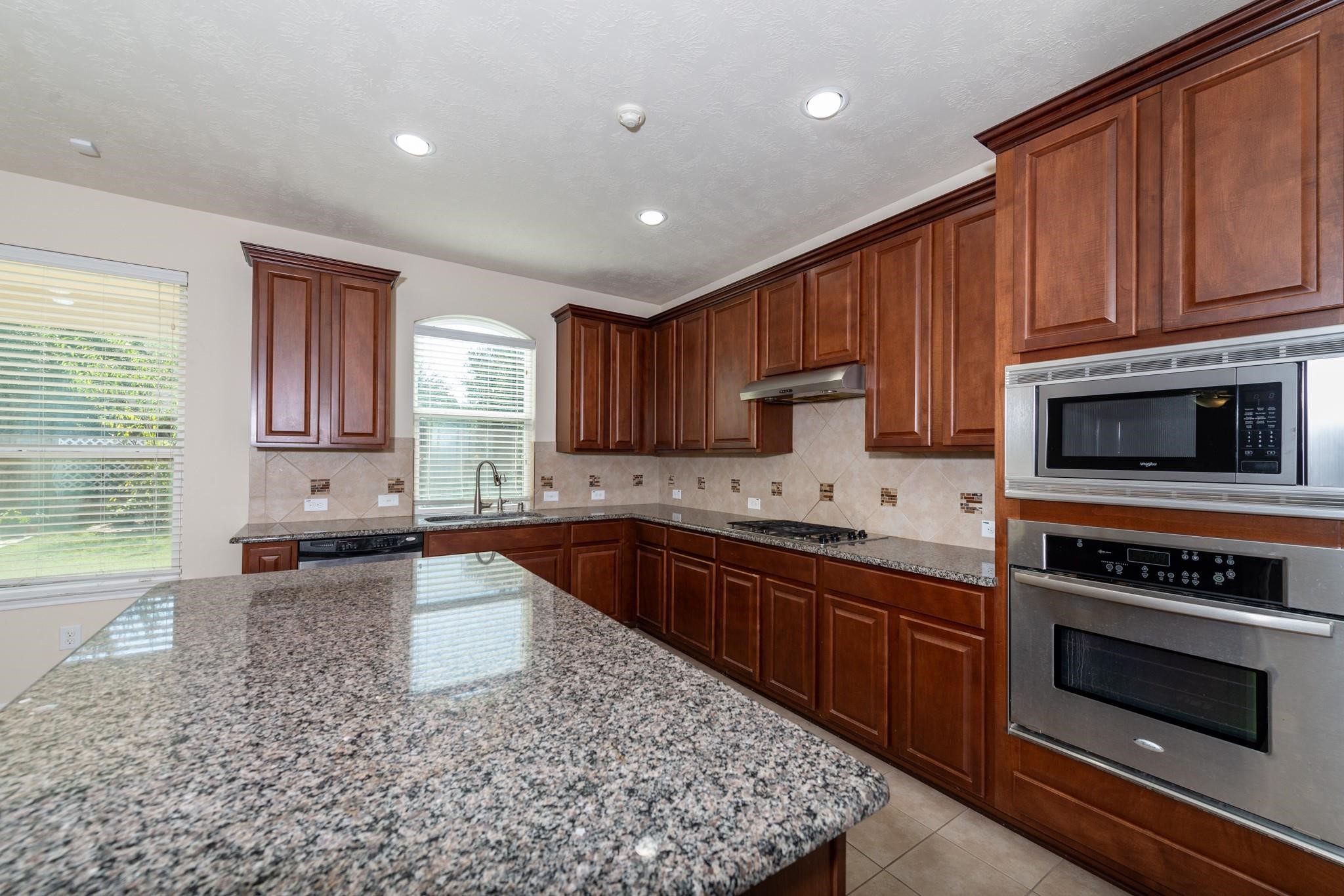 6402 Addlestone Ridge Lane Katy, TX 77494 - Photo 4 of 25 Chef’s kitchen featuring a large granite island, abundant cabinetry, built-in microwave and oven, gas cooktop, and generous counter space. The sink is perfectly positioned beneath a window overlooking the backyard, making meal prep and cleanup a pleasure.