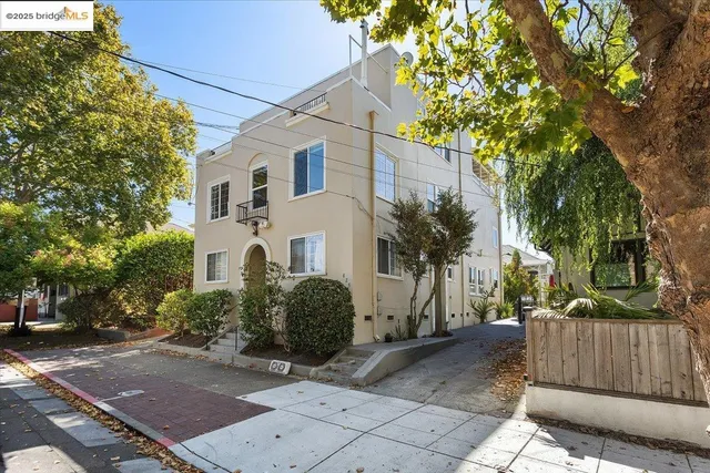 a view of a white house with a large tree and wooden fence