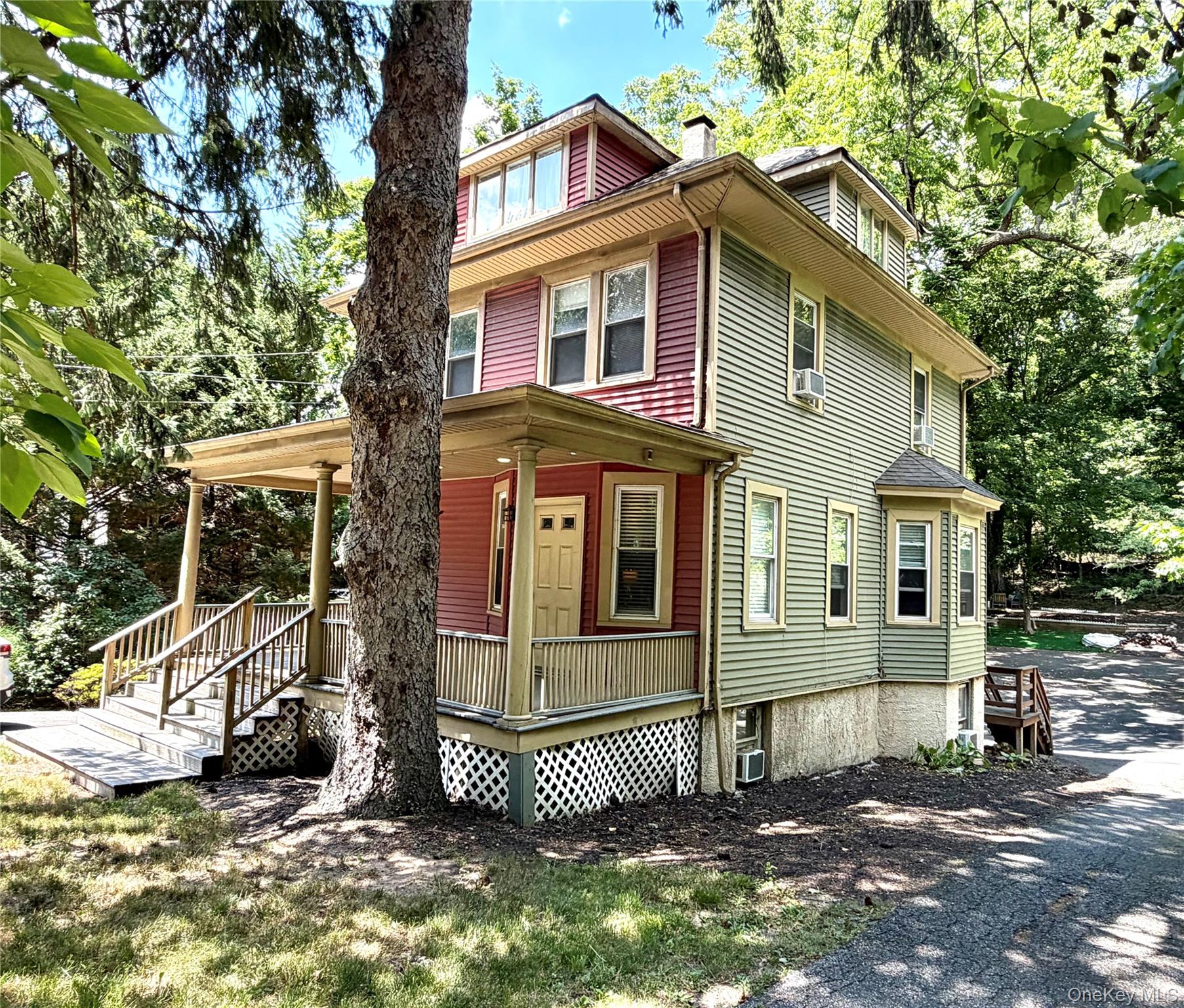149 Fort Salonga Road Northport, NY 11768 - Photo 18 of 23 Multi-level residential property with red and sage green siding, featuring a covered front porch with lattice detailing