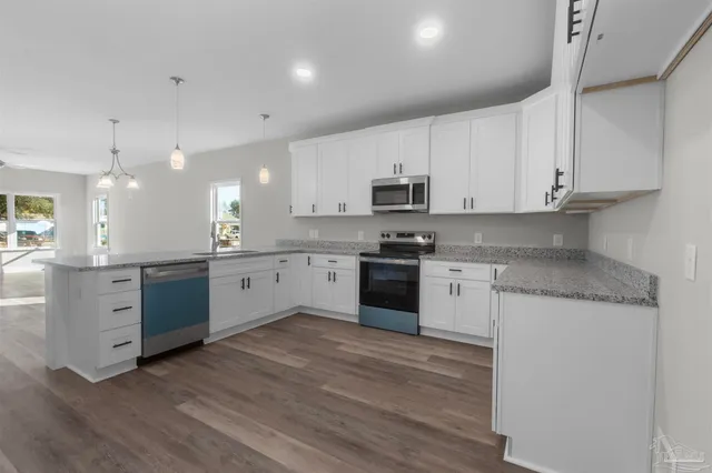 a kitchen with stainless steel appliances granite countertop white cabinets a sink a stove a refrigerator and microwave with wooden floor