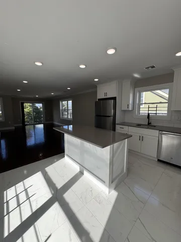 a large living room with stainless steel appliances kitchen island granite countertop a refrigerator a sink dishwasher and a black countertop cabinets