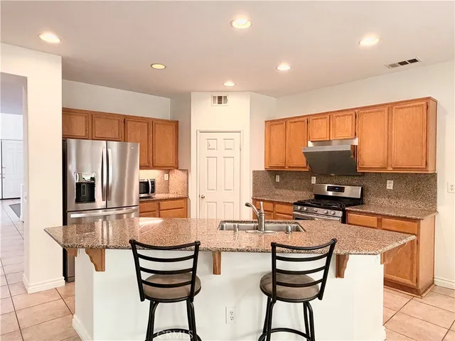 a kitchen with stainless steel appliances granite countertop a stove a sink a refrigerator white cabinets and wooden floor