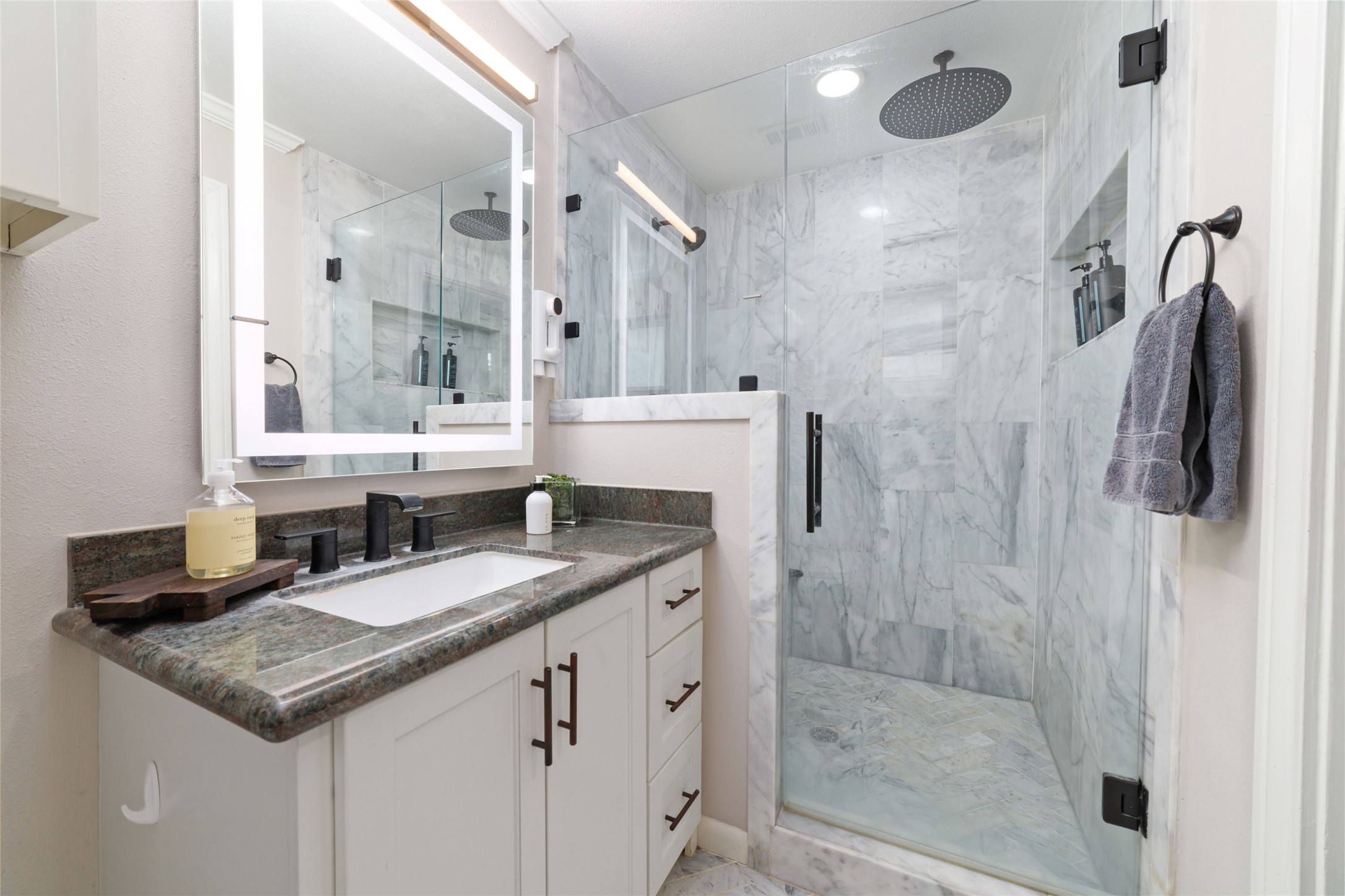 10607 Chimney Rock Road Houston, TX 77096 - Photo 27 of 35 Oversized marble shower with glass wall and door, rain head plus wall head, and a granite seat built in. LED mirror, oversized vanity with drawers and storage, and marble herringbone floors. It’s clean, finished, and done right.