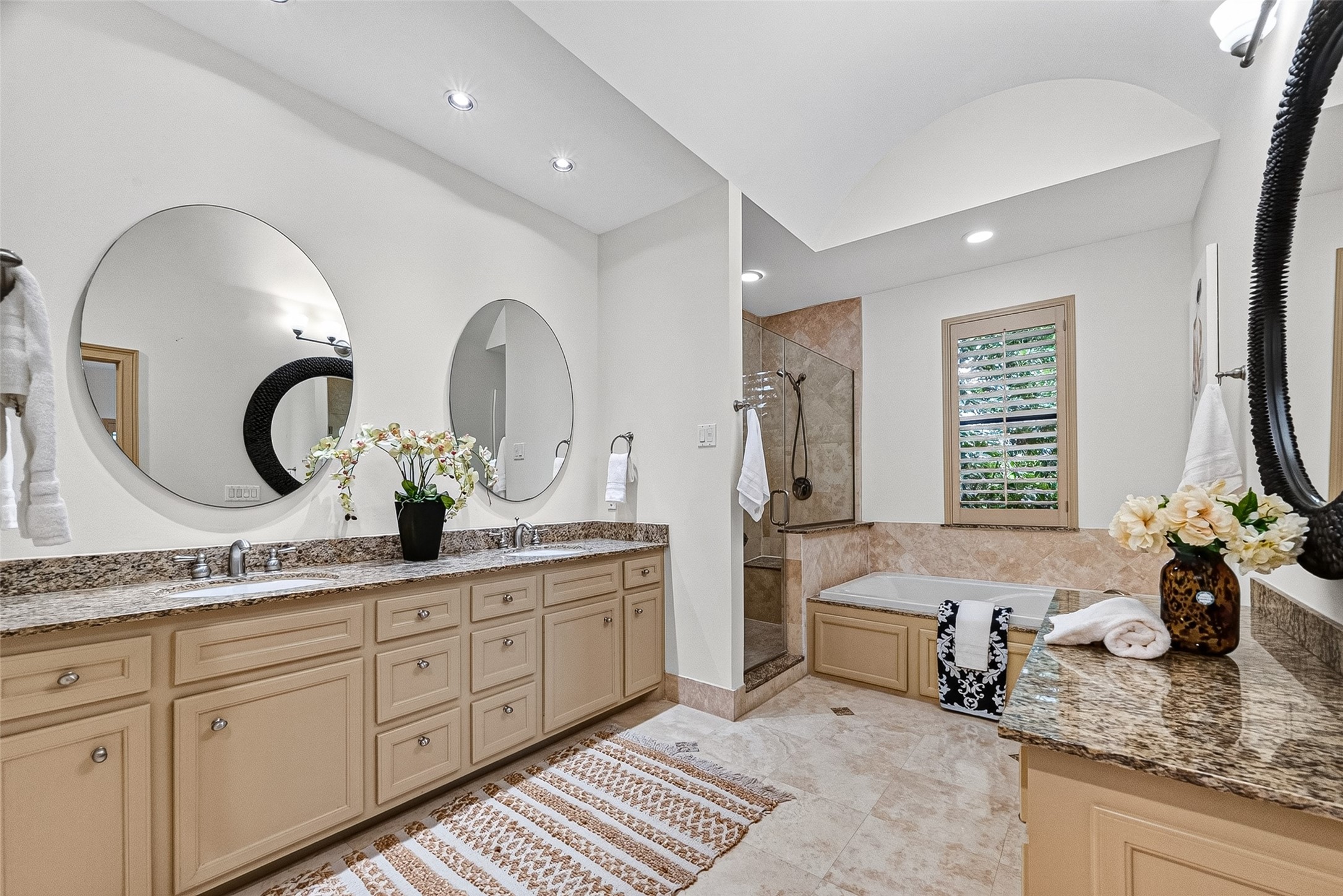 2034 Colquitt Street, Unit A Houston, TX 77098 - Photo 30 of 41 This spacious primary bathroom features dual sinks with granite countertops, large round mirrors, a separate shower, and a luxurious jetted bathtub. The neutral tones and recessed lighting create a relaxing atmosphere, complemented by elegant tile flooring and decorative accents.