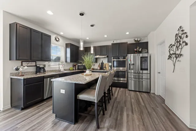 a kitchen with stainless steel appliances kitchen island granite countertop a refrigerator a stove a sink and a oven with wooden floor