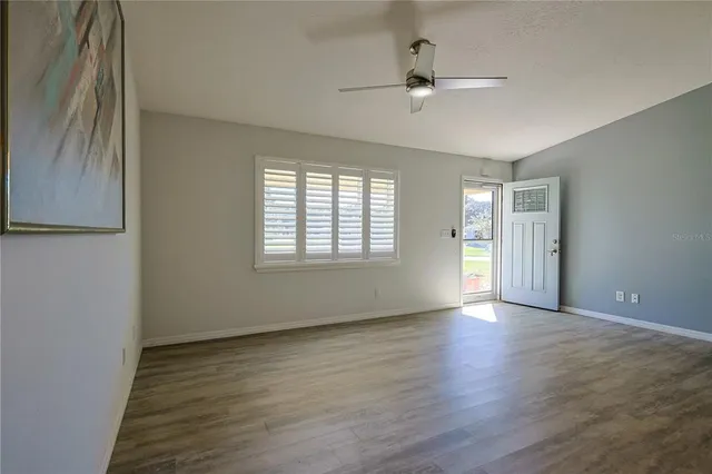 an empty room with wooden floor chandelier fan and windows