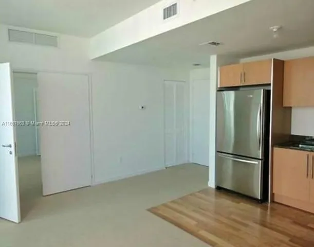 a view of a refrigerator in kitchen and an empty room with wooden floor