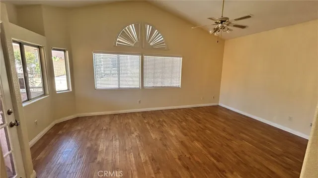 an empty room with wooden floor chandelier fan and windows