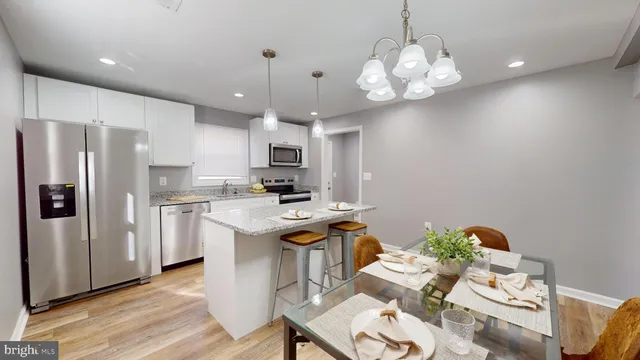 a kitchen with stainless steel appliances granite countertop a refrigerator a sink dishwasher a stove a dining table and chairs with wooden floor