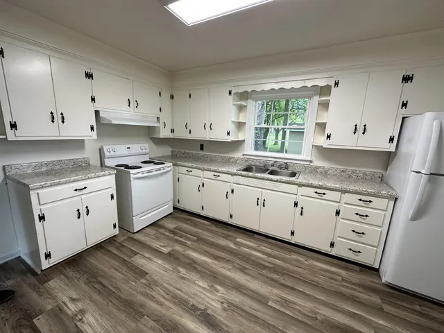 a kitchen with granite countertop white cabinets white appliances a sink and a window