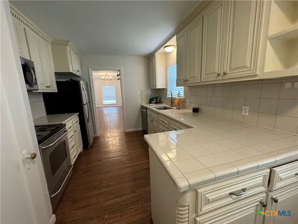 a kitchen with stainless steel appliances a stove a refrigerator a sink a oven with wooden floor and cabinets