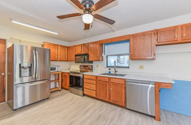 a kitchen with stainless steel appliances granite countertop a refrigerator a sink dishwasher a stove top oven a kitchen island and cabinetry with wooden floor