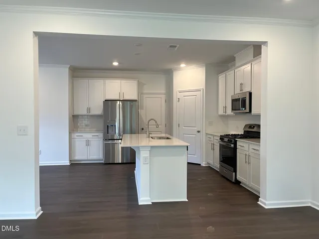 a kitchen with stainless steel appliances a stove top oven a sink a refrigerator white cabinets and wooden floor