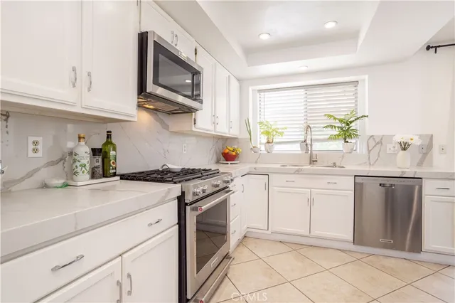 a kitchen with granite countertop white cabinets stainless steel appliances a sink and a window