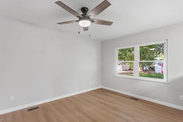 an empty room with wooden floor fan and windows