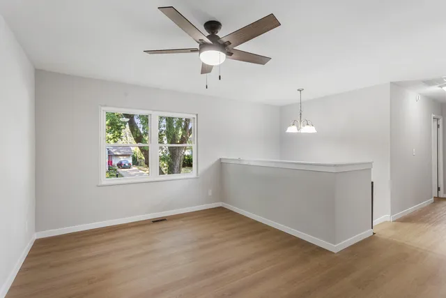 an empty room with wooden floor chandelier fan and windows