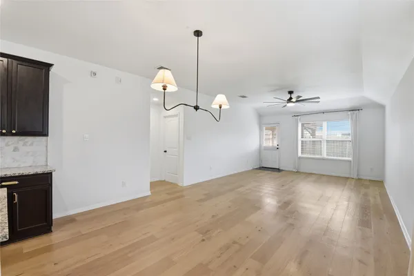 an empty room with wooden floor chandelier fan and windows