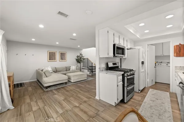 a living room with stainless steel appliances furniture a rug and a kitchen view