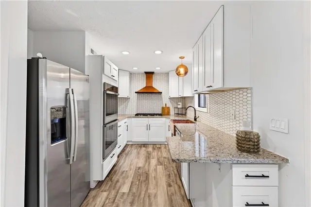 a kitchen with granite countertop a refrigerator a sink and white cabinets