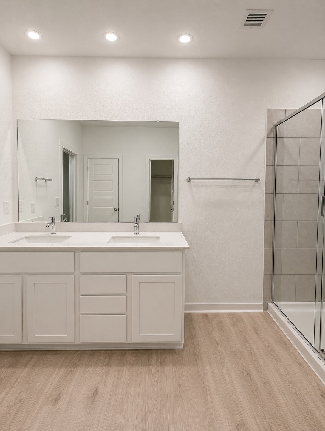 2313 Ranier Court Austin, TX 78754 - Photo 5 of 5 Bathroom featuring a dual vanity with white cabinetry and integrated sinks, a large wall-mounted mirror, a glass-enclosed shower with tiled walls, and wood-finish flooring