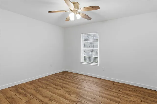 an empty room with wooden floor fan and windows