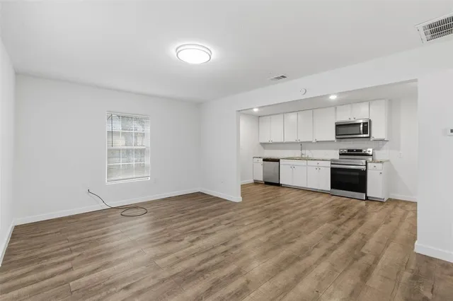 a view of an empty room with kitchen and window