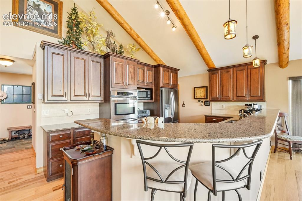 858 Oak Ridge Road Manitou Springs, CO 80829 - Photo 17 of 50 Open concept kitchen with quartz counter tops, matching stainless appliances, rustic cherry cabinetry, a breakfast bar and a wine rack all surrounded by solid hickory flooring