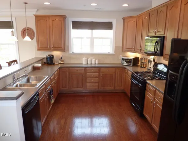 a kitchen with stainless steel appliances granite countertop wooden cabinets a sink a stove a refrigerator and island with wooden floor
