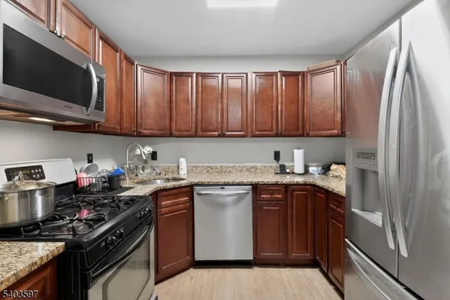 a kitchen with stainless steel appliances granite countertop a stove top oven a sink dishwasher and a refrigerator with wooden cabinets