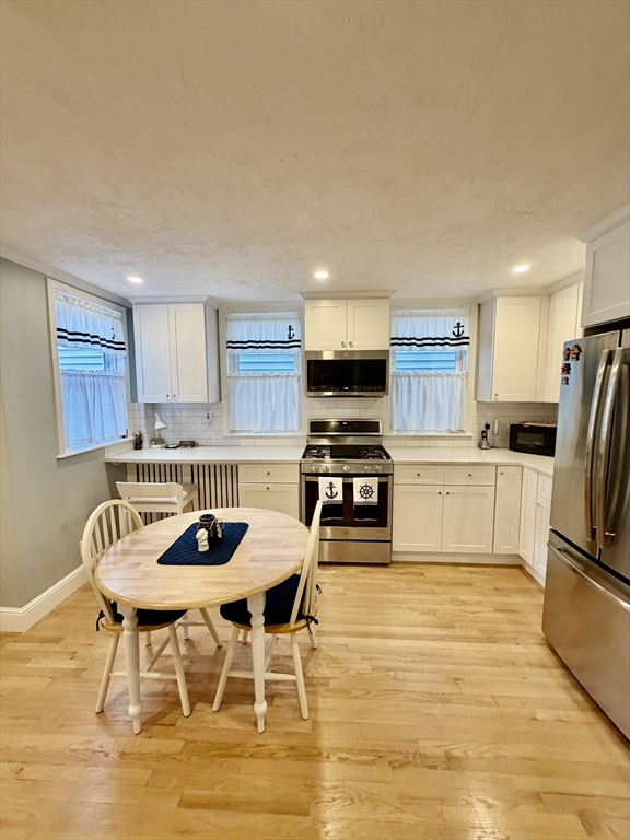 176 M Street, Unit 1 Boston, MA 02127 - Photo 3 of 11 a kitchen with stainless steel appliances kitchen island granite countertop a dining table chairs refrigerator and sink