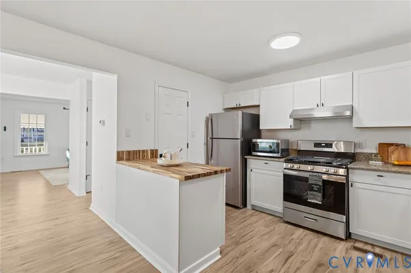 a kitchen with stainless steel appliances granite countertop a stove top oven a refrigerator and white cabinets with wooden floor
