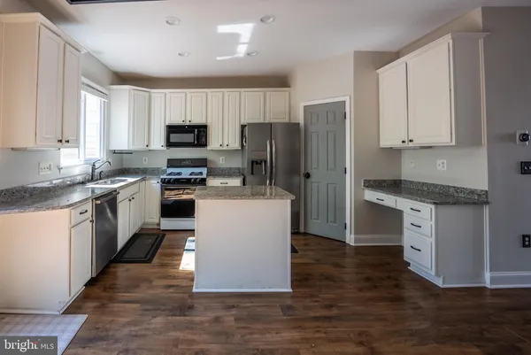 a kitchen with kitchen island granite countertop a stove top oven a sink dishwasher a refrigerator and white cabinets with wooden floor