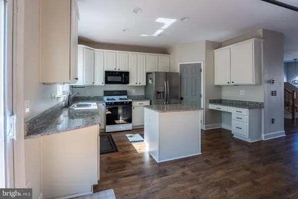 a kitchen with stainless steel appliances granite countertop a stove top oven a sink a refrigerator and white cabinets