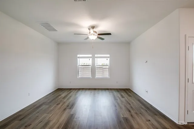 an empty room with wooden floor chandelier fan and windows
