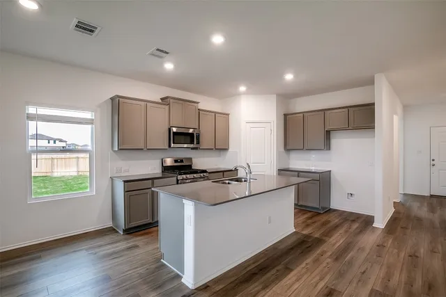 a kitchen with stainless steel appliances granite countertop refrigerator a sink dishwasher a oven with white cabinets and wooden floor